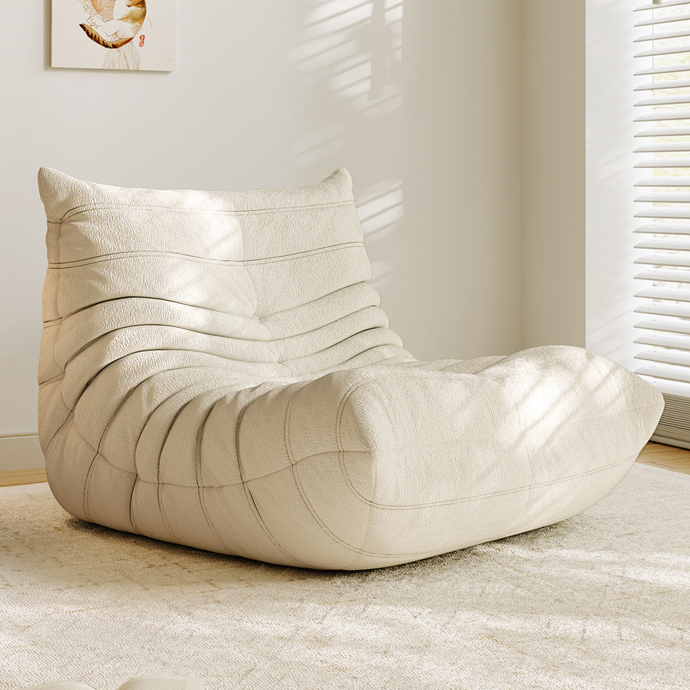 Beige lounge sofa chair with thick padded backrest, arched seat, and quilted wave stitching.